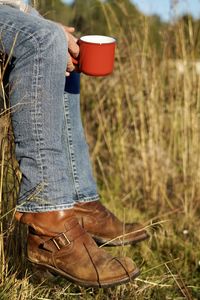 Low section of farmer having coffee while sitting at farm during sunny day