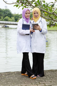 Full length of general practitioner with friend using digital tablet by lake