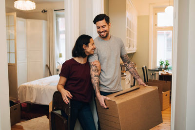 Cheerful woman standing with man carrying box at home
