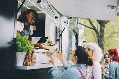 Female owner giving street food to smiling customers in city