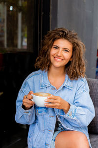 Young charming woman with curly hairstyle having fresh cappuccino with latte art and relaxing alone