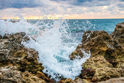Waves splashing on rocks at shore against sky