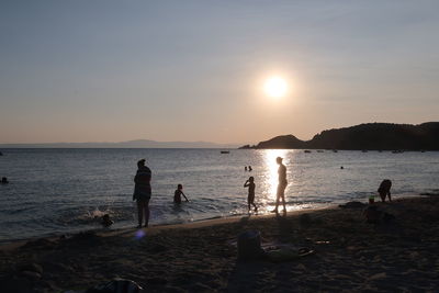 Silhouette people at beach against sky during sunset