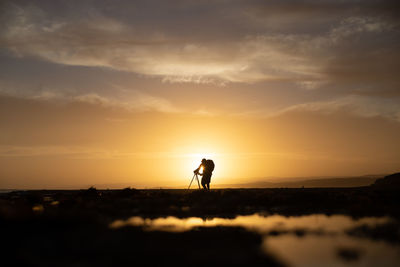 Silhouette man standing on field against sky during sunset