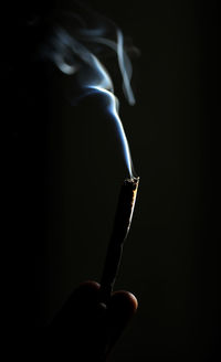 Close-up of hand holding cigarette against black background