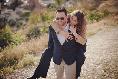 Man giving piggy back ride to happy woman standing on land