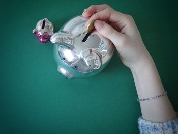 Cropped hand of woman putting coin in piggy bank on table