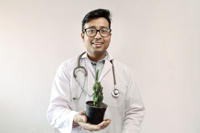 Portrait of doctor holding cactus against white background