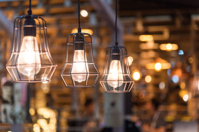 Close-up of illuminated light bulb hanging from ceiling