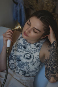 Young woman holding shower head sitting in bathtub