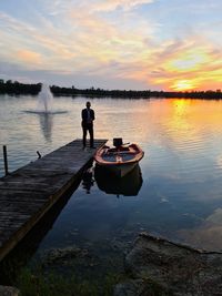 Rear view of man standing on lake against sky during sunset