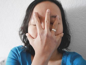 Close-up of woman covering face by white wall