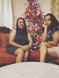 Portrait of smiling young woman sitting by christmas tree