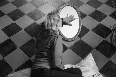 Rear view of woman touching mirror on floor