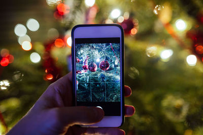Close-up of hand photographing christmas tree at night