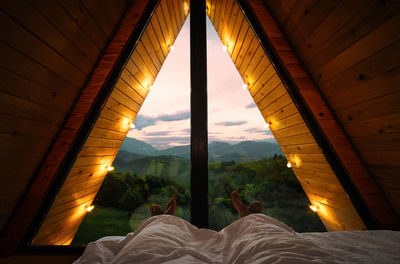 Couple in bed in a-frame cabin looking at sunset on mountain