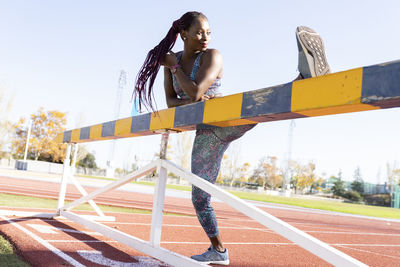 Sportswoman doing warm up exercise on balance beam against clear sky during sunny day