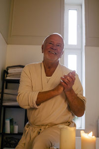 Smiling senior man sitting by lit candle in bathroom at home