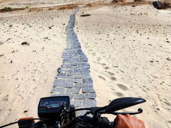 Cropped hand of man riding motorcycle on footpath at desert