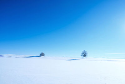 Snow covered landscape against clear blue sky