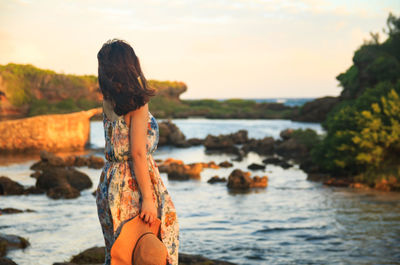 Woman standing on rock at sea shore against sky