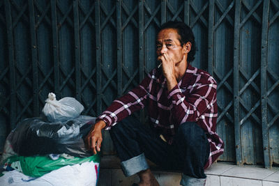 Smoking portrait of man standing by fence against building