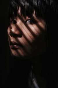 Close-up portrait of serious young woman against black background