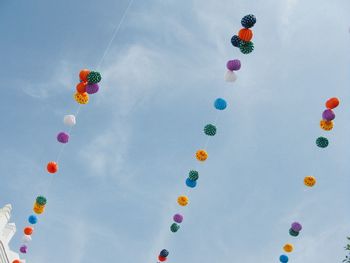 Low angle view of multi colored balloons hanging on strings against sky