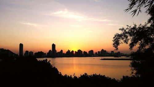 Silhouette of city at waterfront during sunset