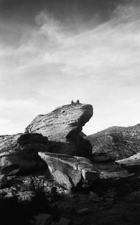 Rock formations on cliff against cloudy sky