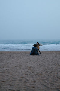 Man sitting on beach against clear sky