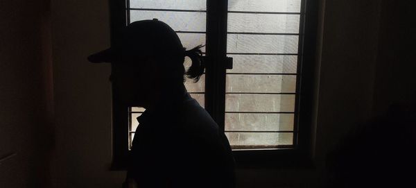 Silhouette woman standing by window at home