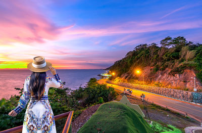 Woman standing by sea against sky during sunset