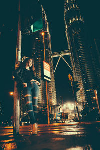 Woman standing against illuminated modern buildings in city