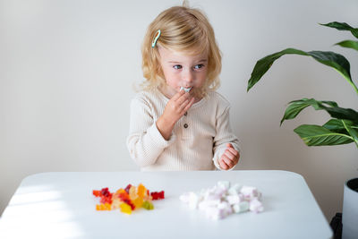 Cute caucasian blonde curly-haired baby girl two, three year old eating jelly, sweet gummy, candy