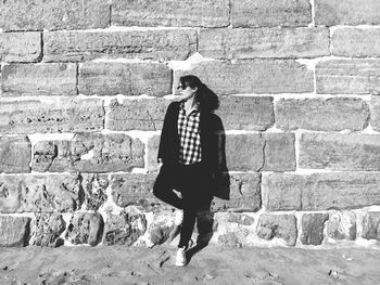 Young woman looking away while leaning on stone wall at beach during sunny day