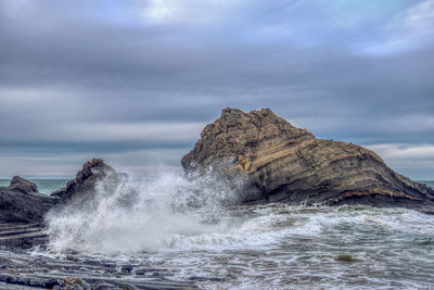 Rock formation hit by waves in sea against sky