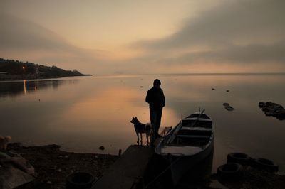 Silhouette man standing with dog by sea during sunset