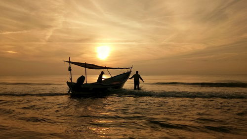 Man in boat on sea against sky during sunset