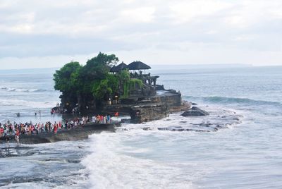 People at pura tanah lot in sea against sky