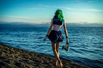 Rear view of woman standing at beach against sky during sunset