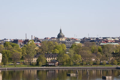 Buildings by trees against clear sky