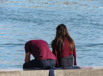 Rear view of couple sitting on retaining wall by sea