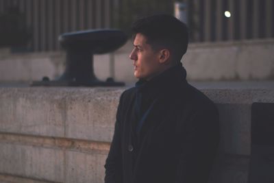 Side view of young man looking away against wall