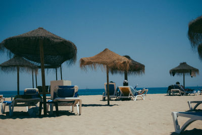 Lounge chairs and parasols on beach against clear blue sky