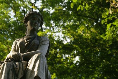 Low angle view of sculpture against trees at cemetery