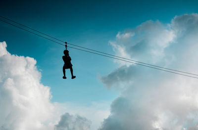 Low angle view of man hanging on rope against sky