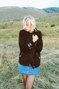 Young woman wearing jacket while standing on grassy field