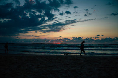 Silhouette people walking on beach against sky during sunset