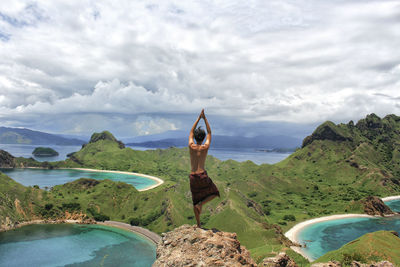 Rear view of man performing yoga while standing on rock against sky